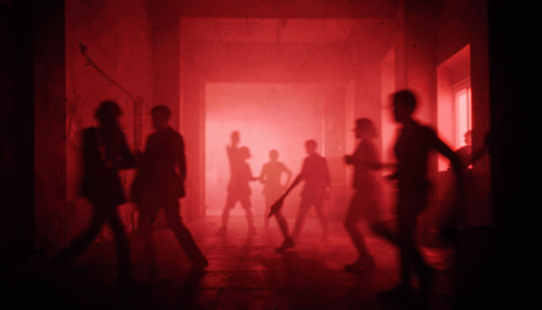 Duotone red-and-black photograph of an atmospheric interior with soft haze and silhouetted figures in motion